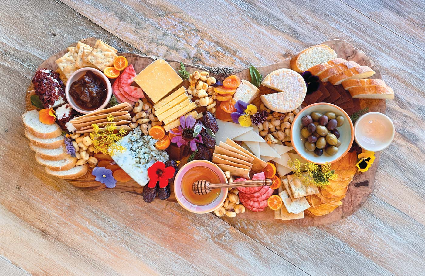 curate cheese board with cheese, fruit, honey, and edible flowers